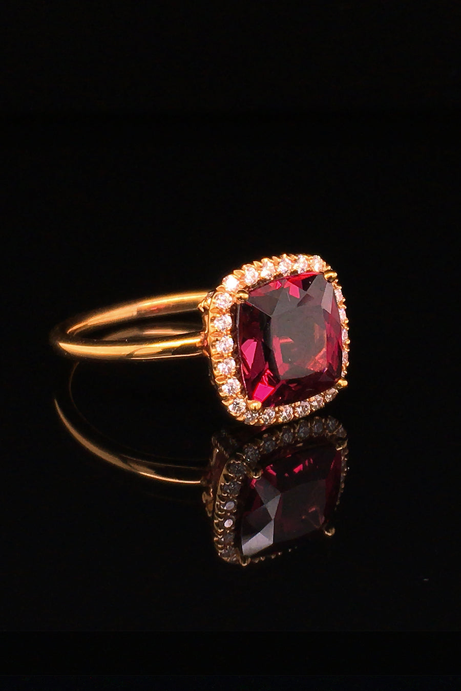 Side view of 20K pink gold ring with a cushion-shaped rhodolite garnet and diamond halo on a black background.