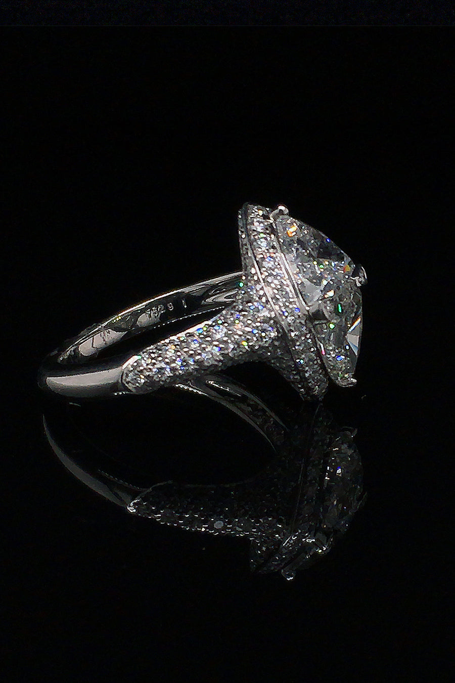 Side view of platinum ring with two trilliants surrounded by pavé diamonds on a black background.