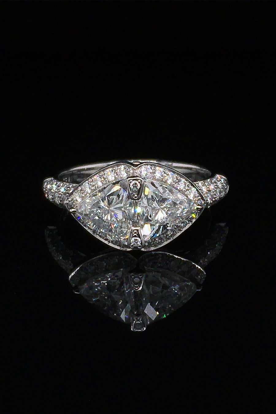 A platinum ring with two trilliant diamonds and brilliant diamonds with  two pink sapphires beneath on a black background.