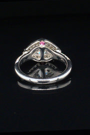 Back view of platinum ring with two trilliants surrounded by pavé diamonds and pink sapphire accents on a black background.
