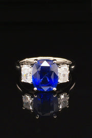 Platinum ring with a blue sapphire and two radiant cut diamonds on either side on black background.