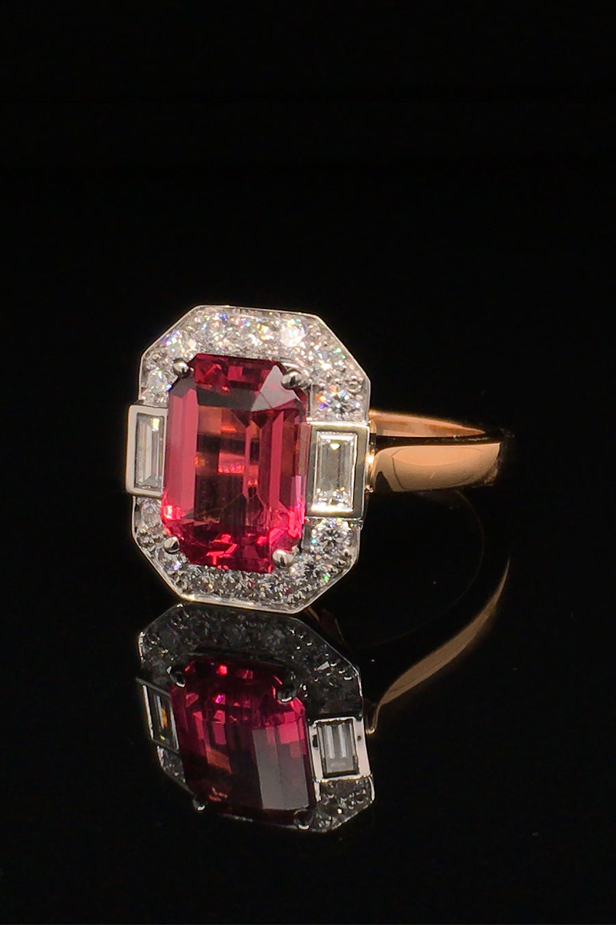 Angle view of rubellite set in platinum with diamonds on 20K pink gold ring on black background.