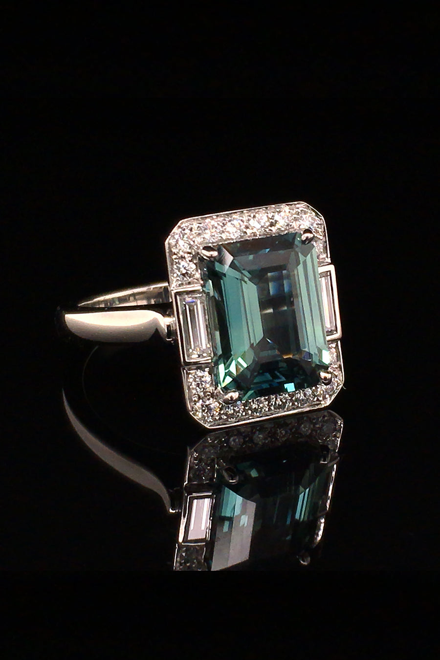 Side view of emerald-cut green sapphire with baguettes and brilliant diamonds in platinum on a black background