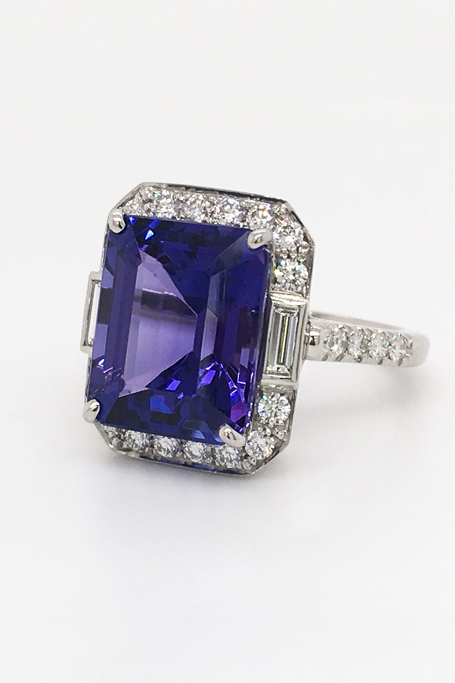 Side view of platinum ring with emerald-cut tanzanite, baguette diamonds, and brilliant diamonds on a white background.