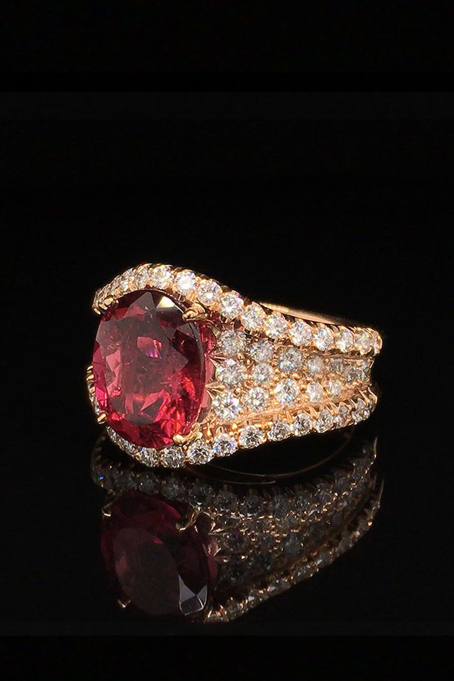 Angle view of 20K pink gold ring with a rubellite and diamond pave on a black background