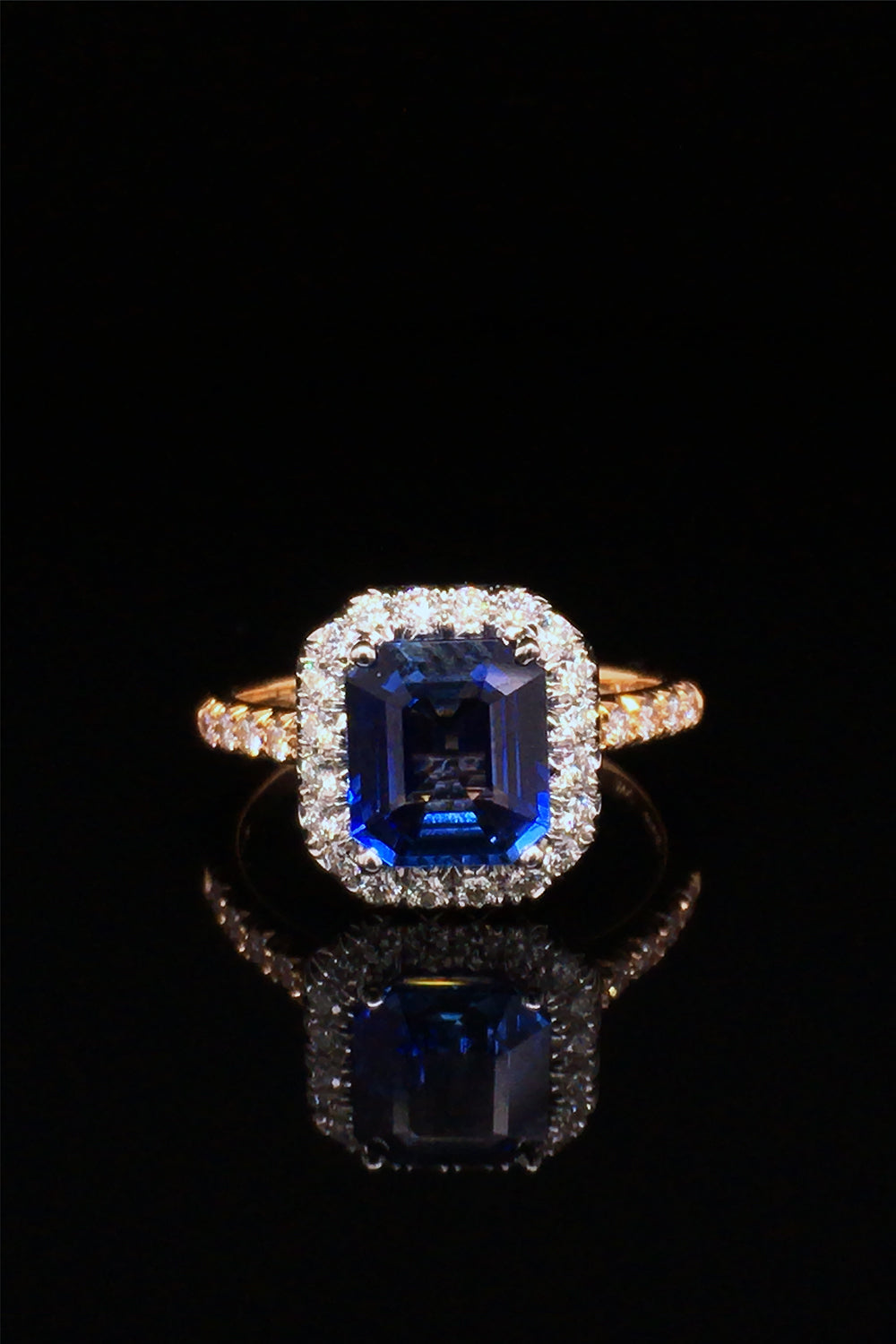 Emerald-cut sapphire set in platinum and surrounded by diamonds with an 18K yellow gold band with diamonds on a black background.