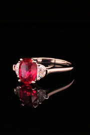 Angle view of platinum ring with oval ruby and two half-moon diamonds on a black background