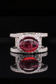 18K white gold ring with an oval rubellite cabochon in a diamond halo between two diamond bands on a black background
