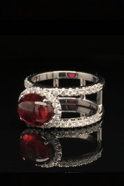 Angle view of 18K white gold ring with an oval rubellite cabochon in a diamond halo between two diamond bands on a black background