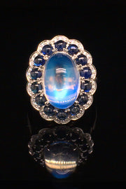 Platinum ring with a large moonstone surrounded by cabochon sapphires and diamonds on a black background