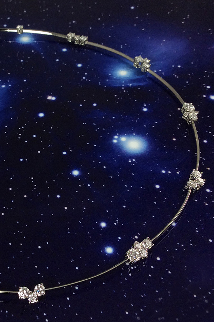Closeup of platinum wire necklace with diamond clusters on a starry background