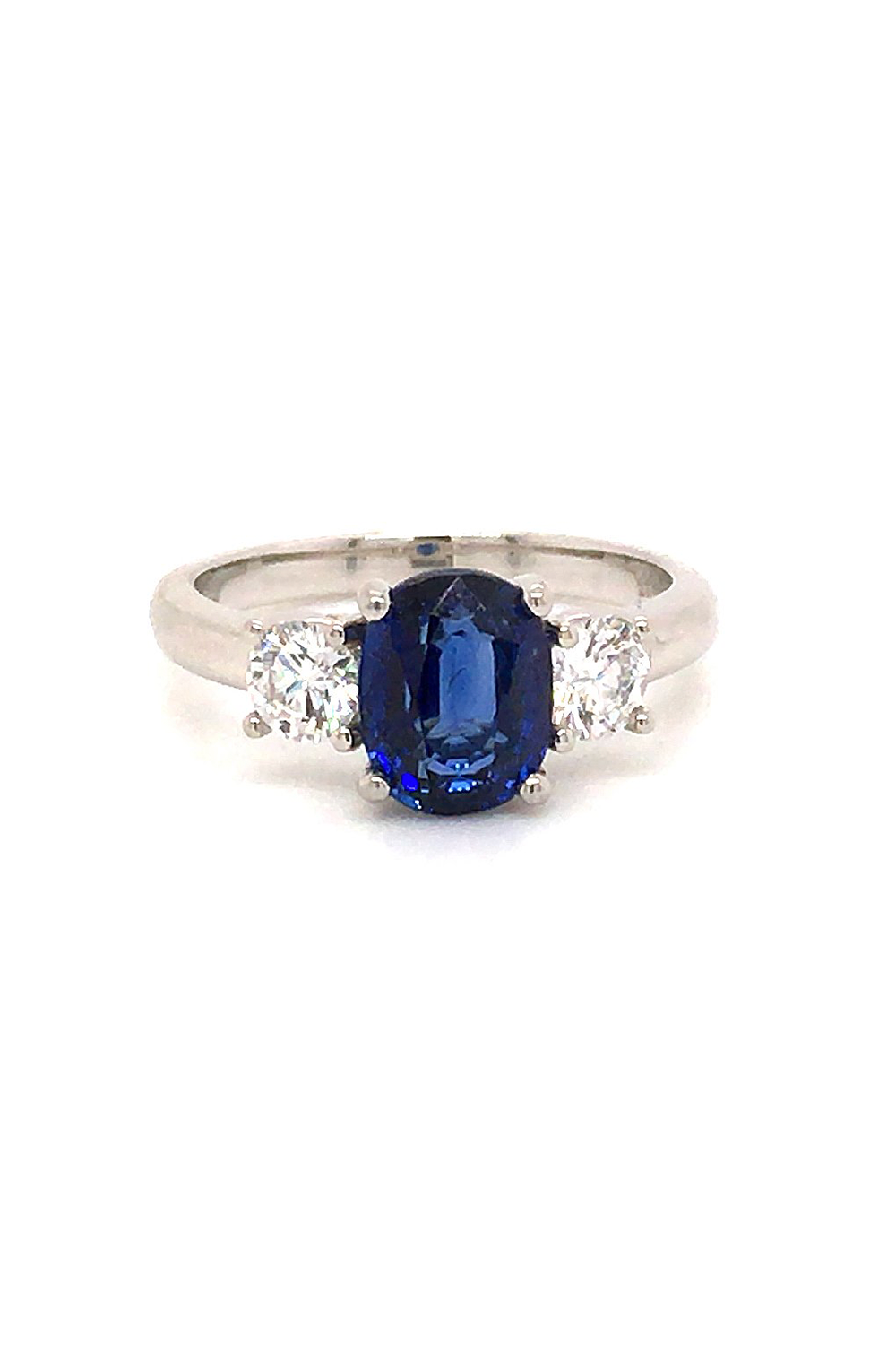 Platinum ring with a blue sapphire and two round diamonds on a white background.