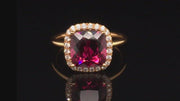 Video of rotating 20K pink gold ring with a cushion-shaped rhodolite garnet and diamond halo on a black background.
