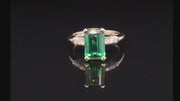 Video of rotating ring with green gemstone and diamonds on black background