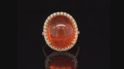 Video of rotating 18K yellow gold ring with orange garnet and diamond halo on black background.