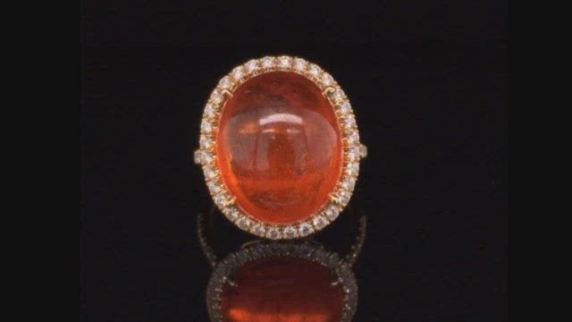 Video of rotating 18K yellow gold ring with orange garnet and diamond halo on black background.