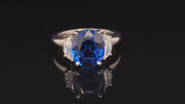 Video of rotating platinum ring with oval blue sapphire and two half-moon diamonds on black background