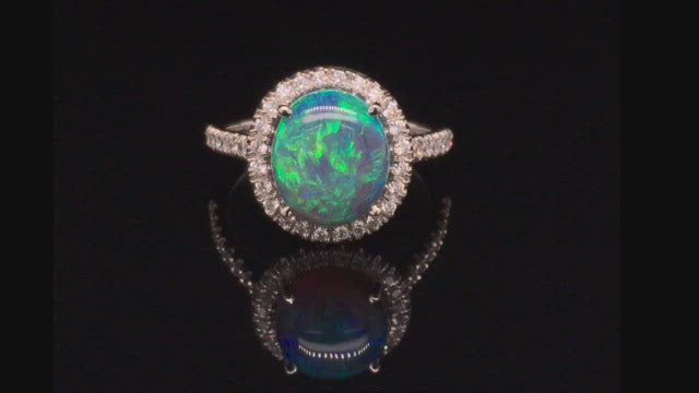 Video of rotating platinum ring with a black opal and diamond halo on a black background.