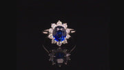 Video of rotating platinum ring with an oval blue sapphire surrounded by brilliant diamonds on black background.