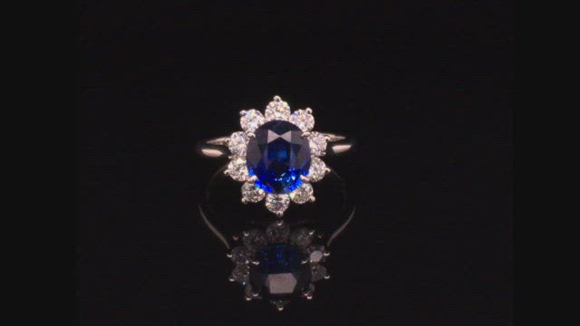 Video of rotating platinum ring with an oval blue sapphire surrounded by brilliant diamonds on black background.