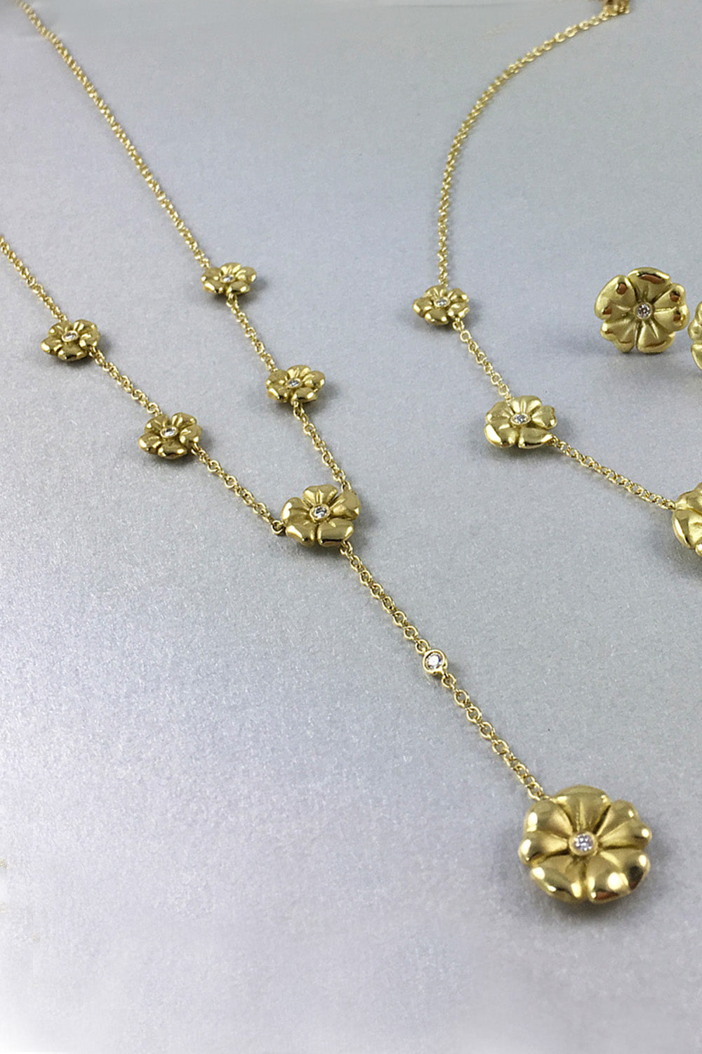 18K yellow gold lariat necklace with flowers, each with a single diamond, on a gray background