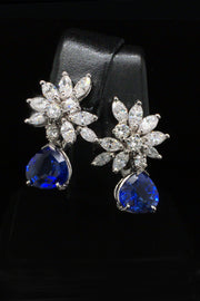 Platinum earrings with a diamond cluster with pear-shape sapphire drops on black background