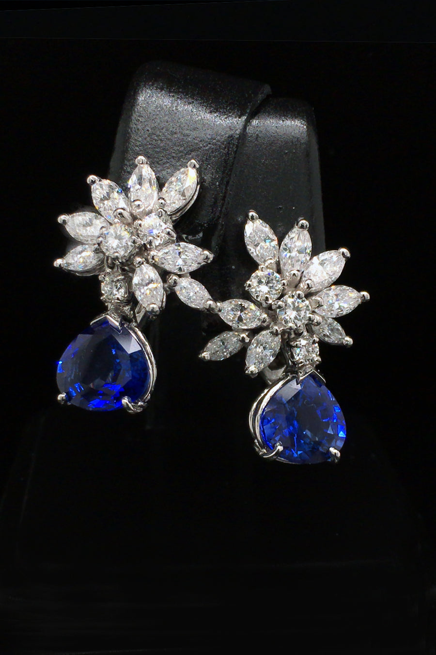 Platinum earrings with a diamond cluster with pear-shape sapphire drops on black background