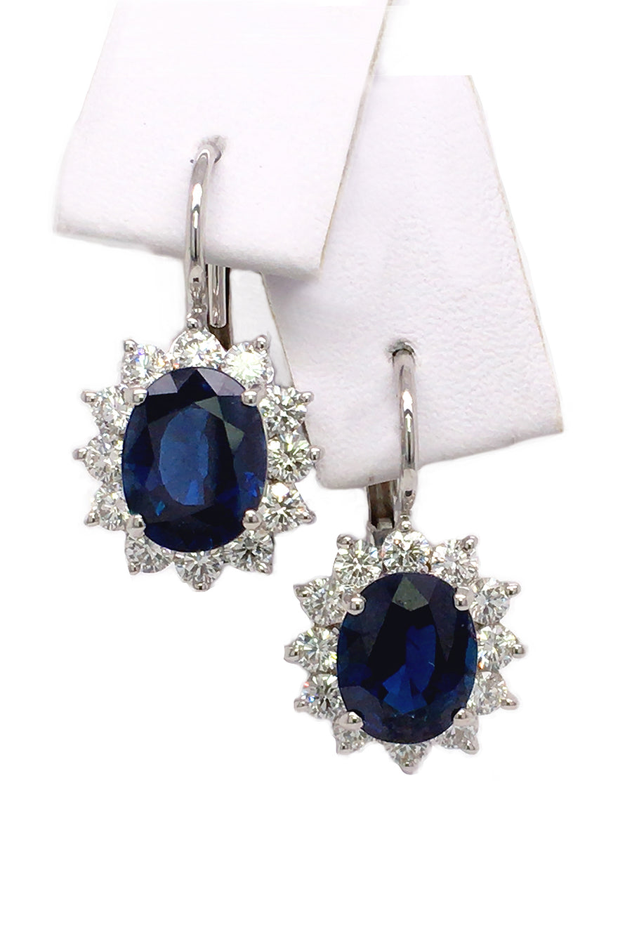 18K white gold earrings with oval blue sapphires surrounded by diamonds on white background