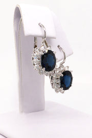 Angle view of 18K white gold earrings with oval blue sapphires surrounded by diamonds on white background