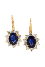 18K yellow gold earrings featuring oval blue sapphires surrounded by smaller diamonds with lever back closures.
