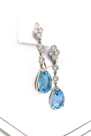 Angle view of platinum drop earrings featuring pear-shaped aquamarines suspended from diamond lace detailing on a white jewelry display