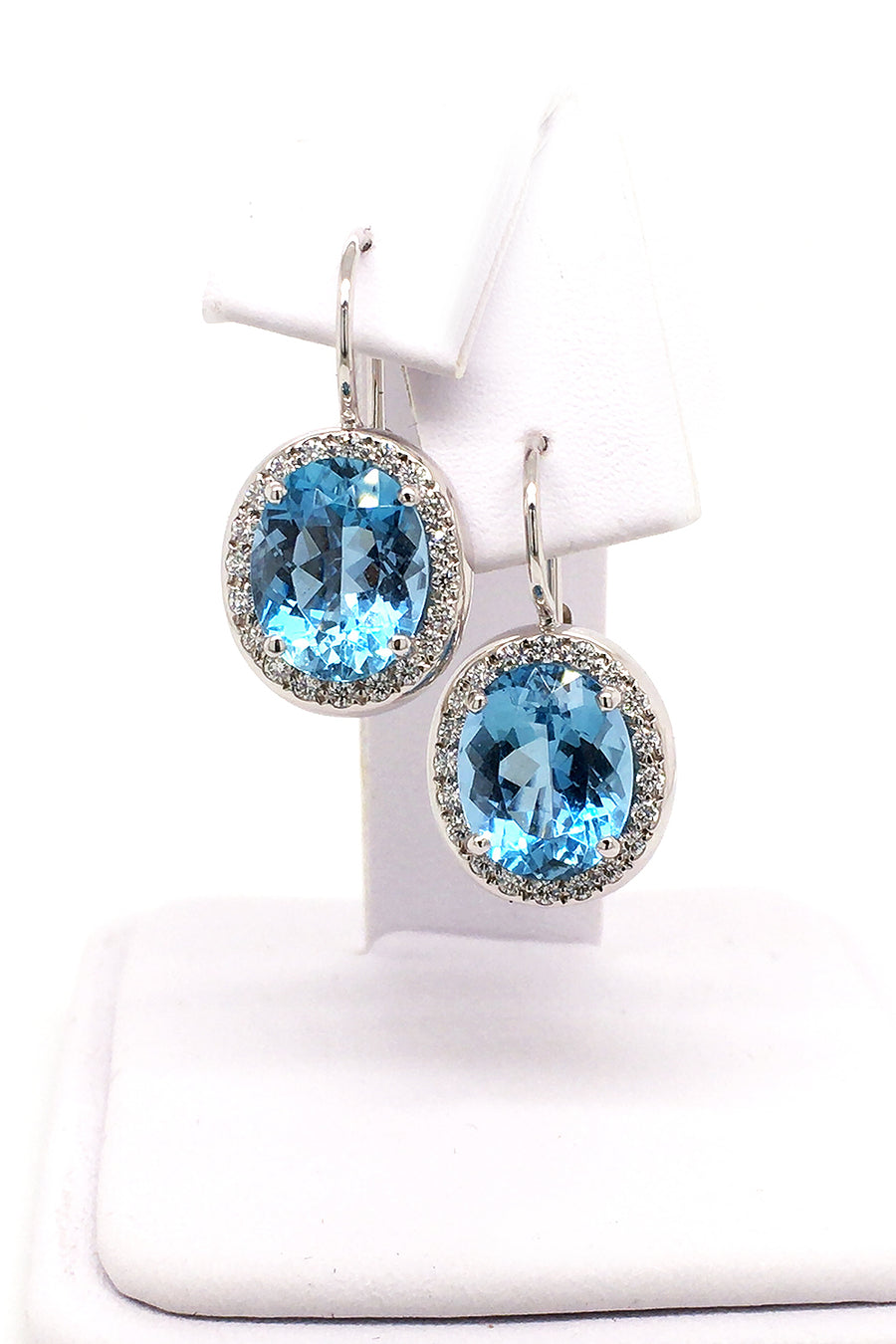 18K white gold earrings featuring large oval aquamarines surrounded with diamonds with lever backs on a white jewelry display