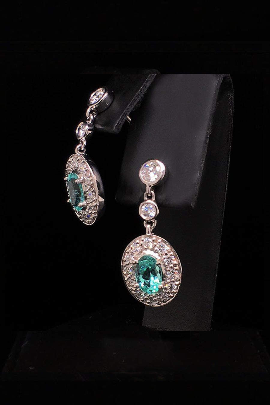 Angle view of platinum earrings with African paraibas and diamonds diamonds on a black background