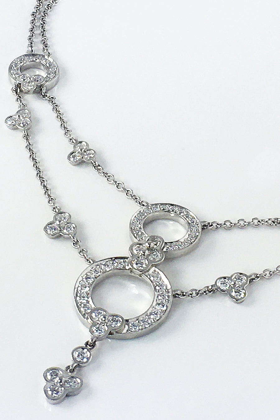 Close-up of a platinum necklace with lace-inspired motif with diamonds on a white background.