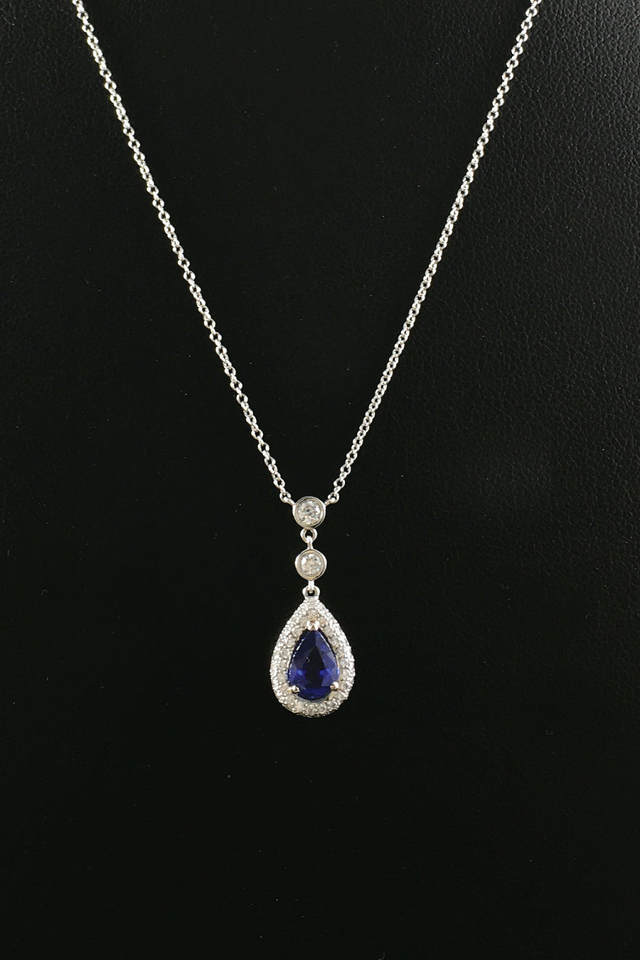 Pear-shaped blue sapphire and diamond necklace in platinum on black background.