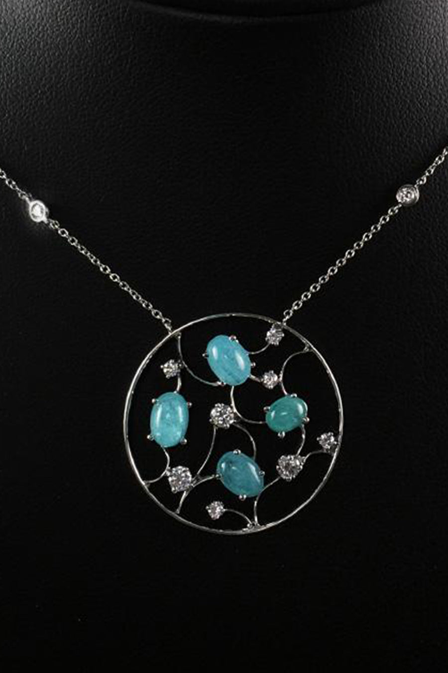 Circular platinum pendant with mosaic motif and Brazilian paraiba cabochons and on a black neck display