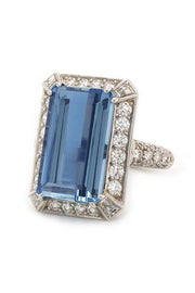 An emerald-cut aquamarine with round diamonds set in a platinum  on a white background