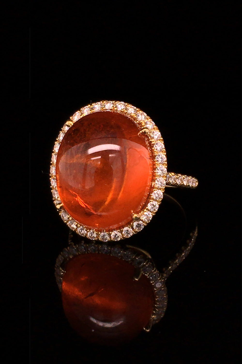 Angle view of 18K yellow gold ring with orange garnet and diamond halo on black background.
