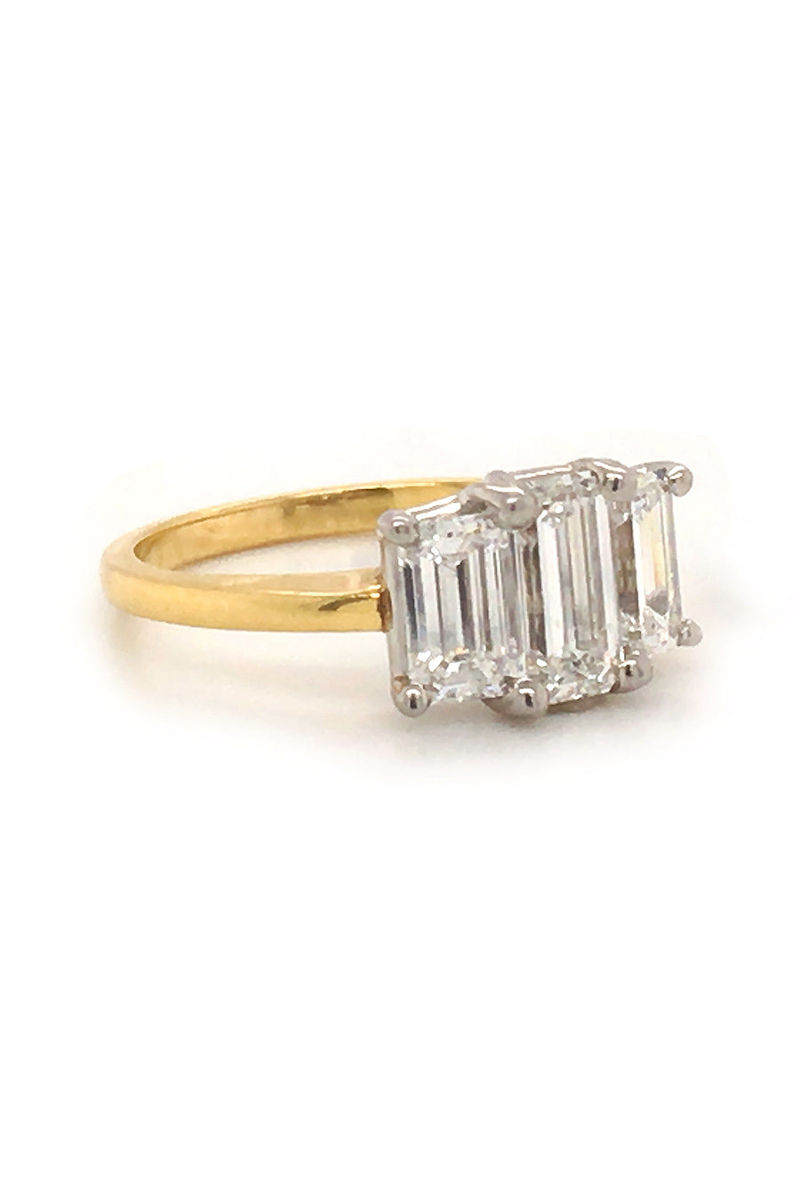 Side view of 18K yellow gold and platinum ring with three emerald-cut diamonds on white background