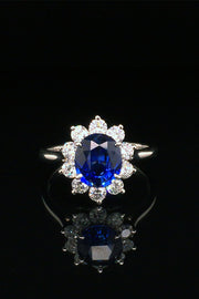 Platinum ring with an oval blue sapphire surrounded by brilliant diamonds on black background.