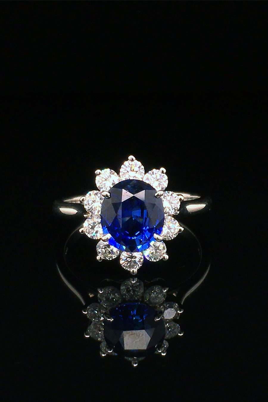 Platinum ring with an oval blue sapphire surrounded by brilliant diamonds on black background.
