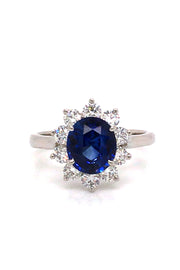 Platinum ring with an oval blue sapphire surrounded by brilliant diamonds on white background.