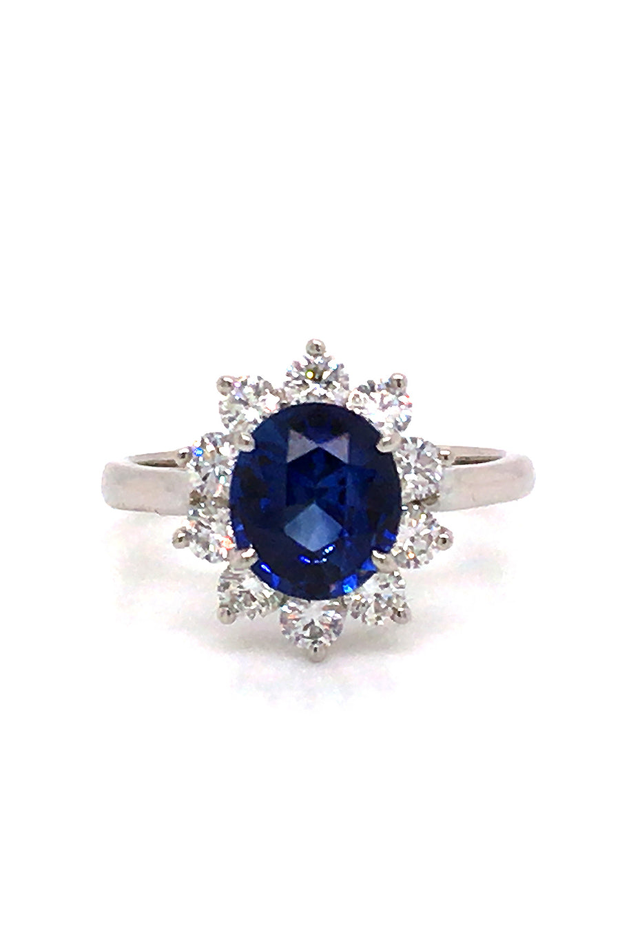 Platinum ring with an oval blue sapphire surrounded by brilliant diamonds on white background.