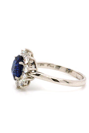 Side view of platinum ring with an oval blue sapphire surrounded by brilliant diamonds on white background.