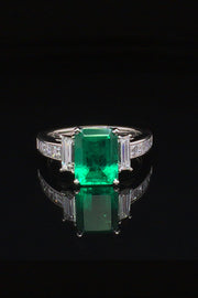 Platinum ring with an emerald, baguette diamonds, and square diamonds on a black background