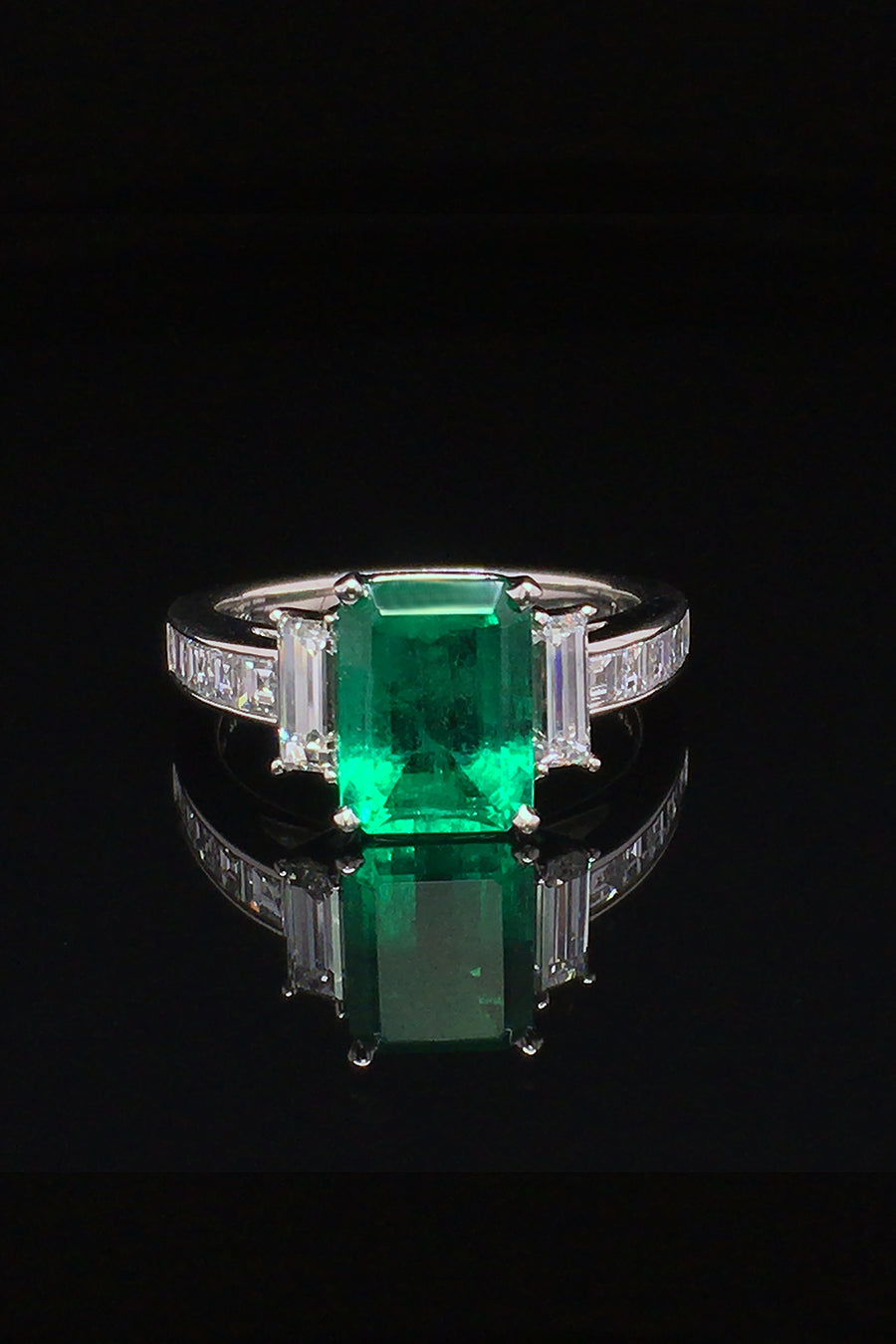 Platinum ring with an emerald, baguette diamonds, and square diamonds on a black background