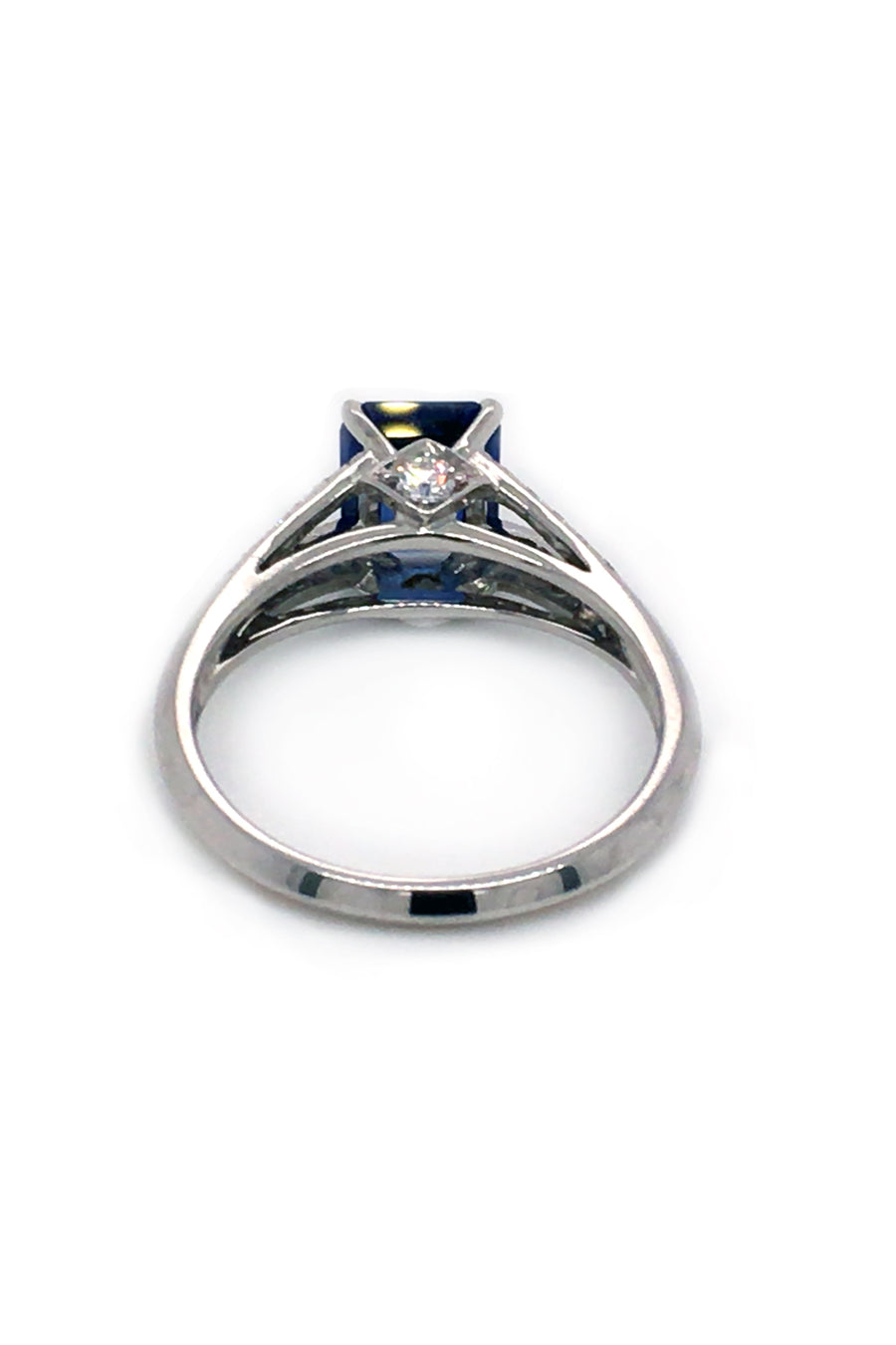 Back view of platinum ring with emerald-cut sapphire and diamonds on white background