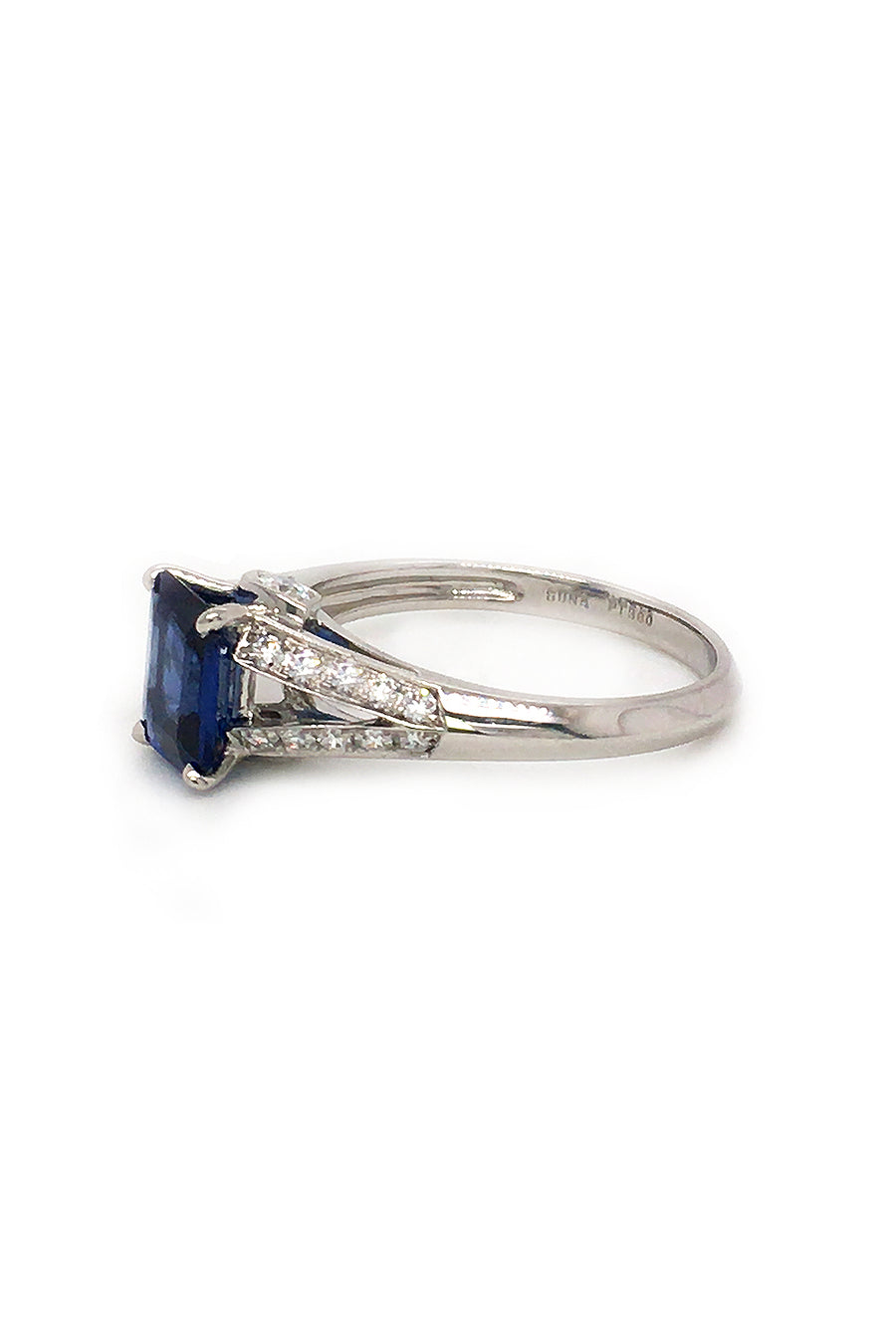 Side view of platinum ring with emerald-cut sapphire and diamonds on white background