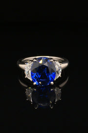 Platinum ring with oval blue sapphire and two half-moon diamonds on black background.