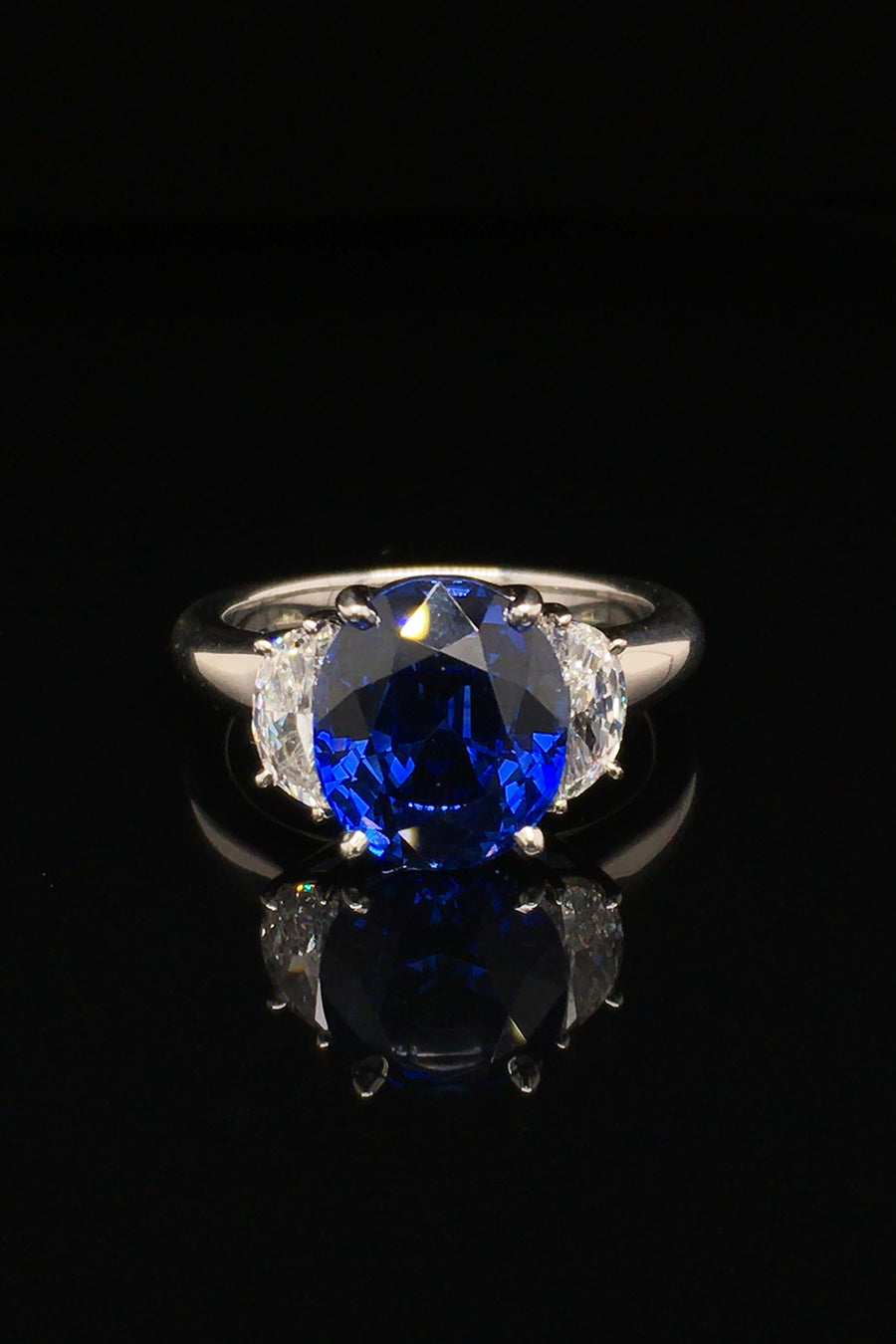Platinum ring with oval blue sapphire and two half-moon diamonds on black background.